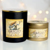Two Victoria Goddess 'Brigid Goddess' soy wax candles, one in a large black glass jar with a gold lid and one in a smaller gold tin, both with matching labels, set against a soft white background with warm bokeh lights.