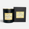 A black soy wax candle with a gold-rimmed top and a textured beige label reading 'CANCER Spring FREEBIA', shown next to its black gift box on a light gray background.