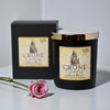 Black candle with gold lid labeled 'Crone' next to a pink rose on a white surface.