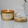 Candle in a tin labeled 'Crone Goddess' with a lit flame on a white surface.