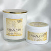 Two Victoria Goddess Kuan Yin Lotus Vanilla soy wax candles, one in a tall glass jar with a gold lid and one in a white plastic jar, both with matching lids, set against a soft white draped background.