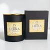 A black soy wax candle jar with a gold rim and a beige label reading 'LIBRA Zodiac' stands next to its matching black box on a light gray background.