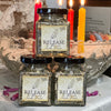 Three jars of 'Release to Renew' herbal incense on a table with lit candles in the background.