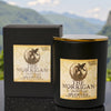 Black candle labeled 'The Morrigan' with packaging against a mountainous background