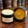 Two black soy wax candles labeled 'Victorian Library' on a wooden table, with one candle open to show the golden wax inside and the other standing closed in the foreground.