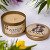 Scented candle in a decorative tin with 'Wench' branding on a white background with flowers.